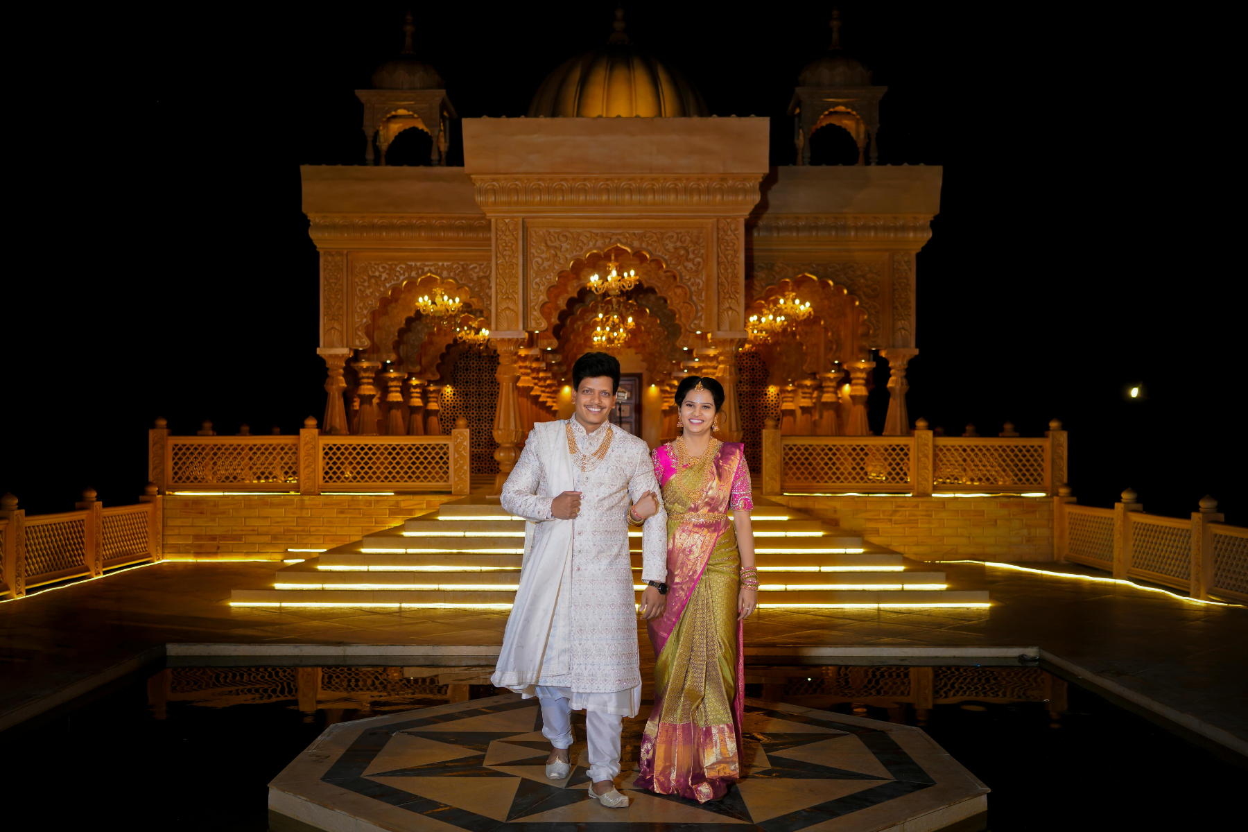 Indian bride and groom in traditional attire posing at a beautifully lit heritage venue at night during their wedding celebration in Delhi NCR.